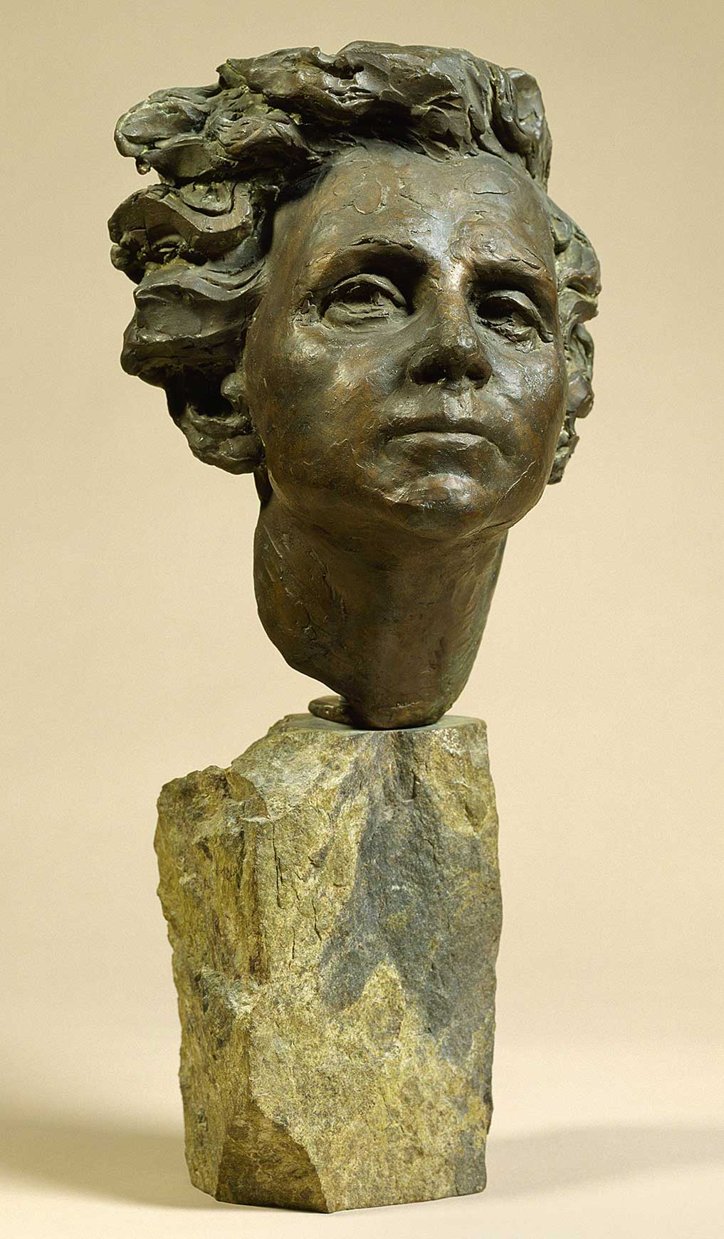 A bronze bust of a woman with flowing hair set on a marble slab