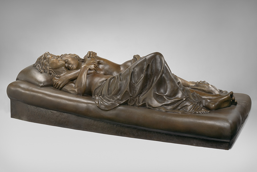 Bronze sculpture of two women on a bed, naked except for blanket in lover's embrace