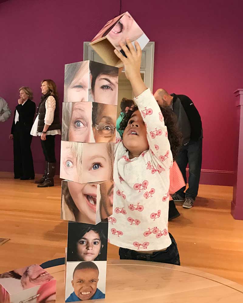 Chlld stacking blocks -- each block has a photograph of part of someone's face.