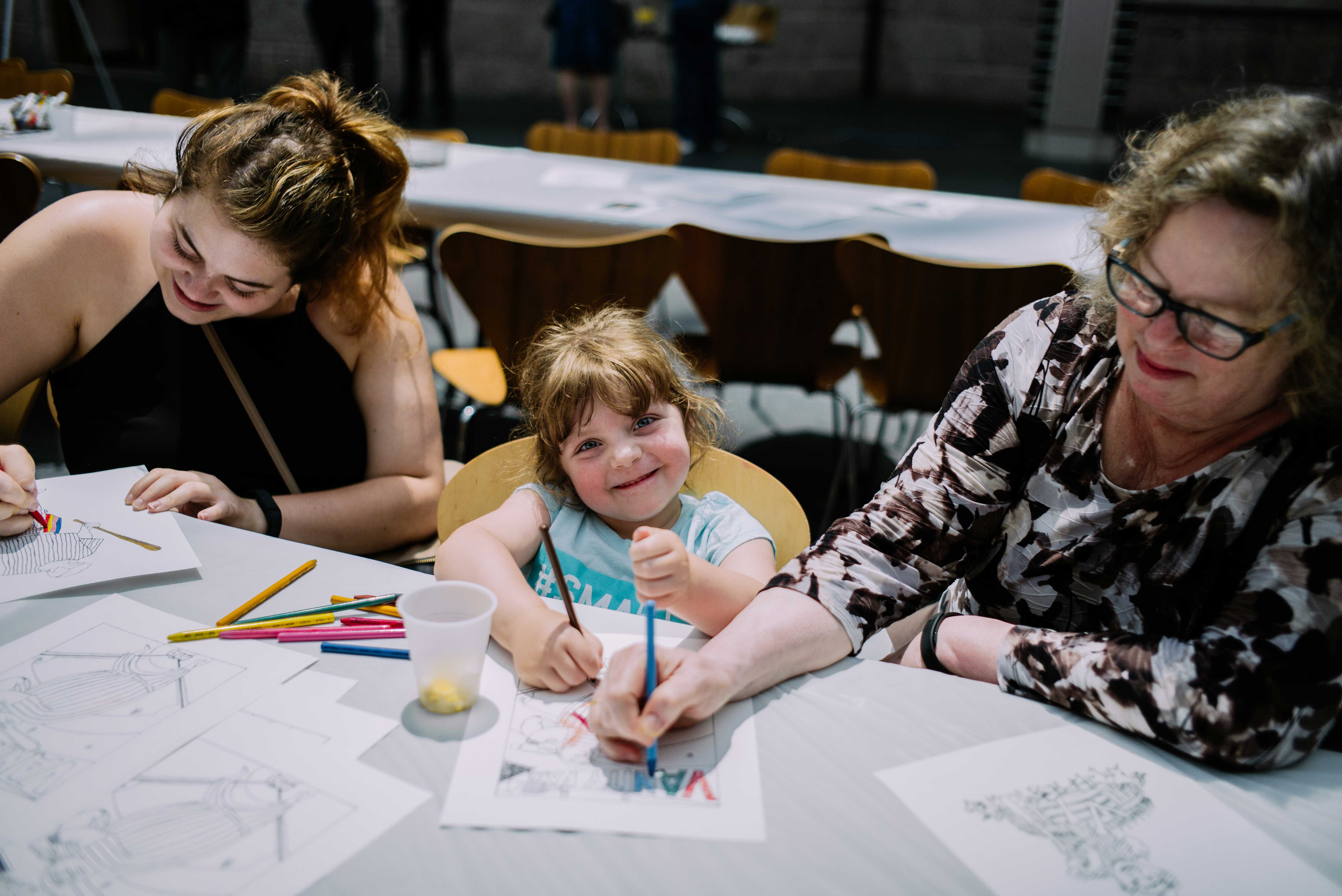Photograph of two woman and a small girl coloring at a table and smiling