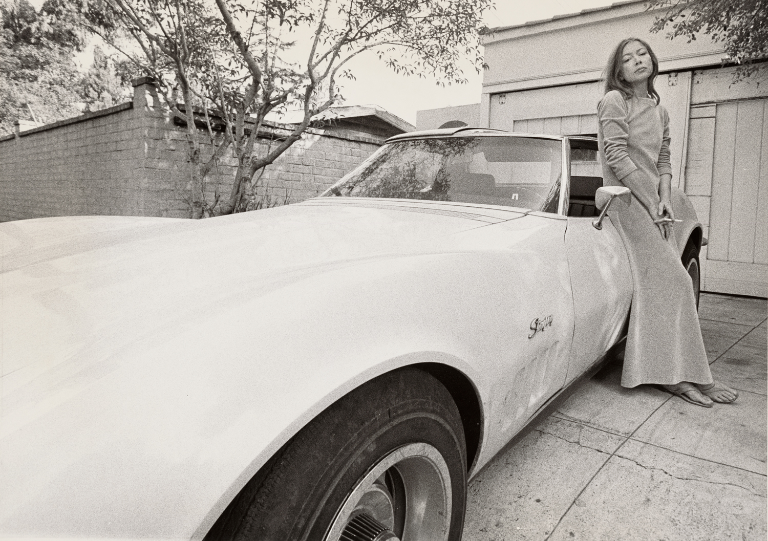 A black and white image of a woman leaning against a car