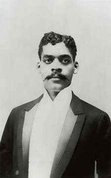 Photo of a man with dark hair and moustache  in a tuxedo 
