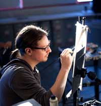 Color photo of David Kassan from right, wearing glasses, as he paints.