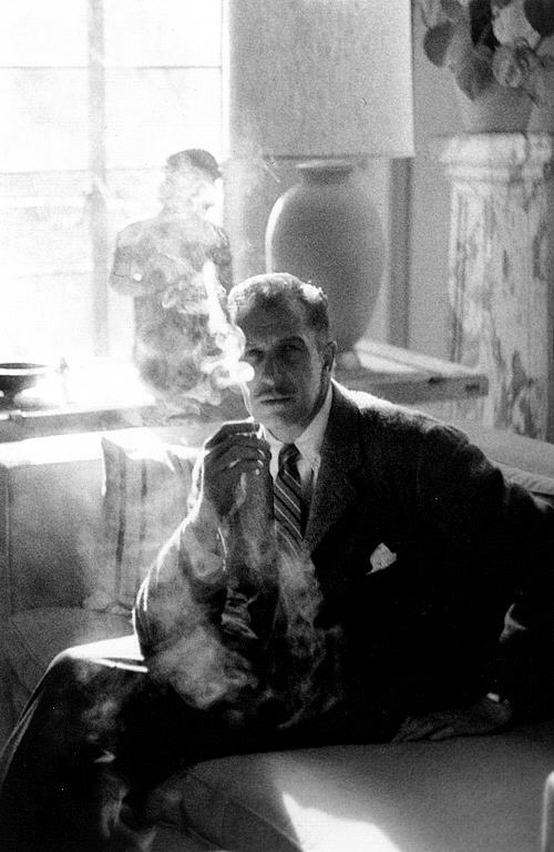 Photograph of a man seated and smoking a cigarette