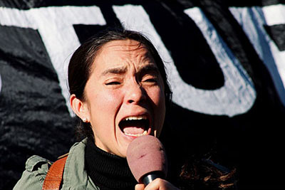 Asian woman shouting into a microphone at a protest rally