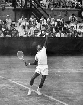 Black and white photo of Arthur Ashe. He is tossing the ball for his serve, at a tennis match