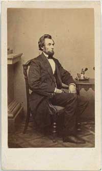 Photograph portrait of Lincoln in formal clothing and sitting at a small table