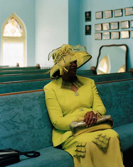 Older African American woman in yellow-green dress and hat, sitting in an empty church 