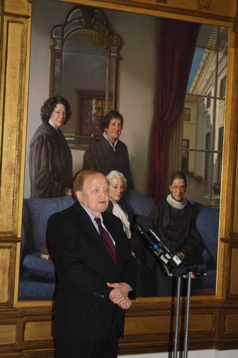 Artist Nelson Shanks in a black suit and red tie speaking into a microphone in front of his painting The Four Justices.