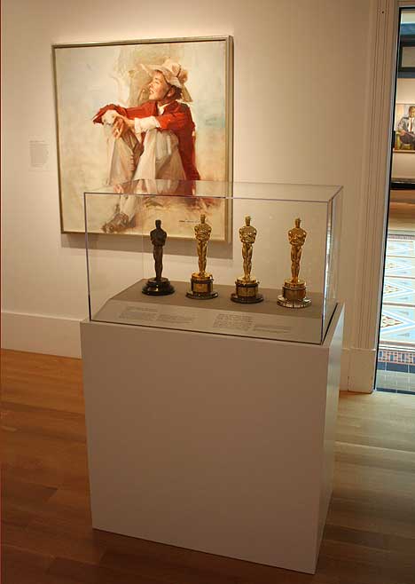 Color photo of Katharine Hepburn's four Academy Awards and her portrait by Everett Raymond Kinstler, in an exhibition.