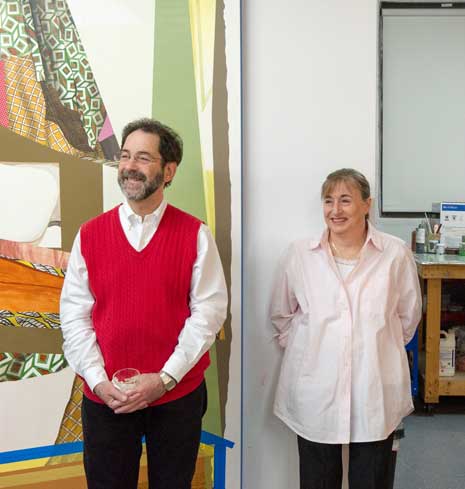 Richard and Fran Morris Rosman, smiling, standing in a room side-by-side, next to a painting