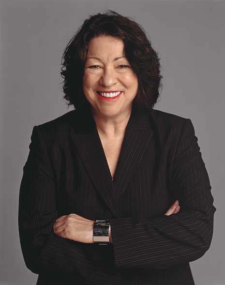 Sonia Sotomayor in black formal shirt and with arms crossed, looking straight into camera smiling