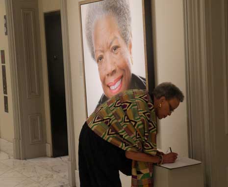 Color photo of a woman signing a visitor comment book next to Maya Angelou's portrait.