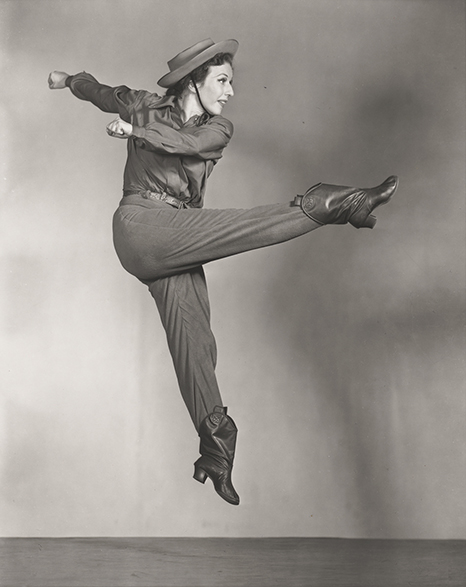Blog_demille Black and white photo of dancer Agnes de Mille on stage, jumping with right leg forward, from right.
