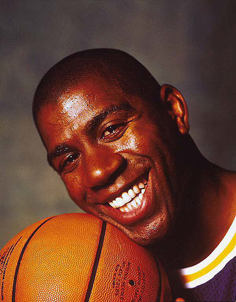 Magic Color photo of Magic Johnson in his Lakers basketball uniform holding a basketball, from front.