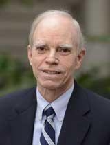 Color photo of Jim Barber from the shoulders up, wearing a blue suit jacket and blue striped tie.
