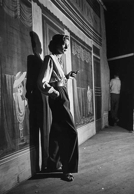 Blog_cool_lauren_bacall Lauren Bacall standing on stage in front of a backdrop, from right, with a cigarette in her left hand.