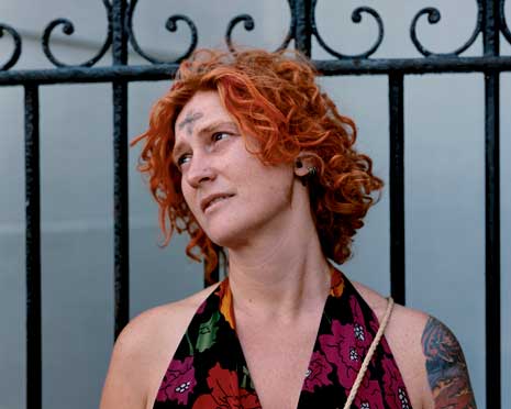 Woman with red curly hair in front of iron gates with ash cross on her forehead