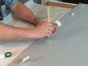 Close-up of hands, pasting down the hinges onto mounting board