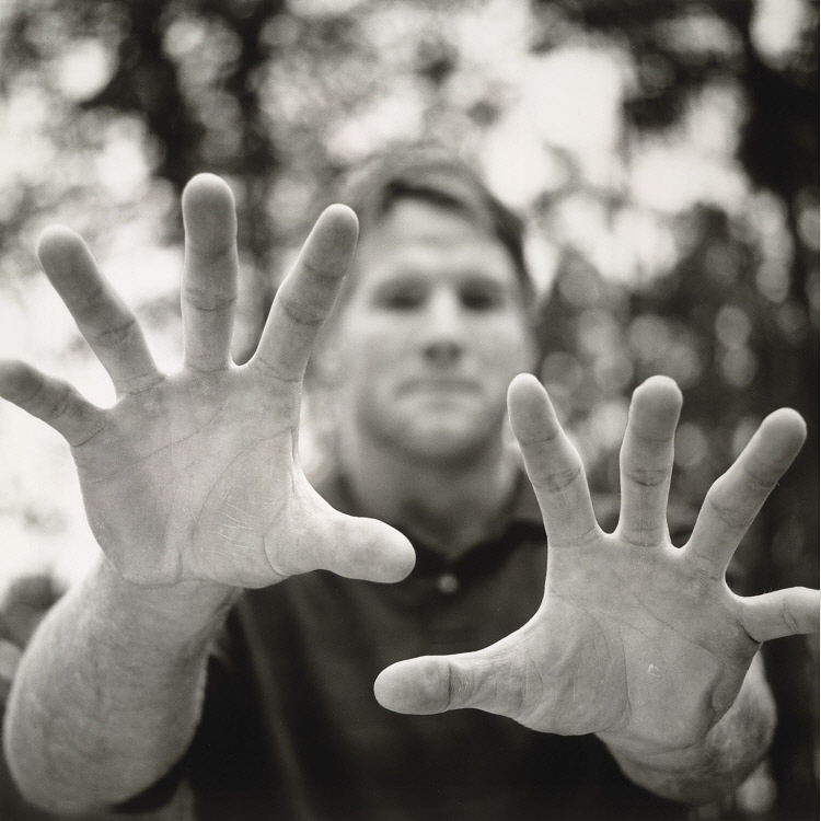 Black and white photograph portrait of Brett Farve, focusing on his outstreched hands, with his face in the background