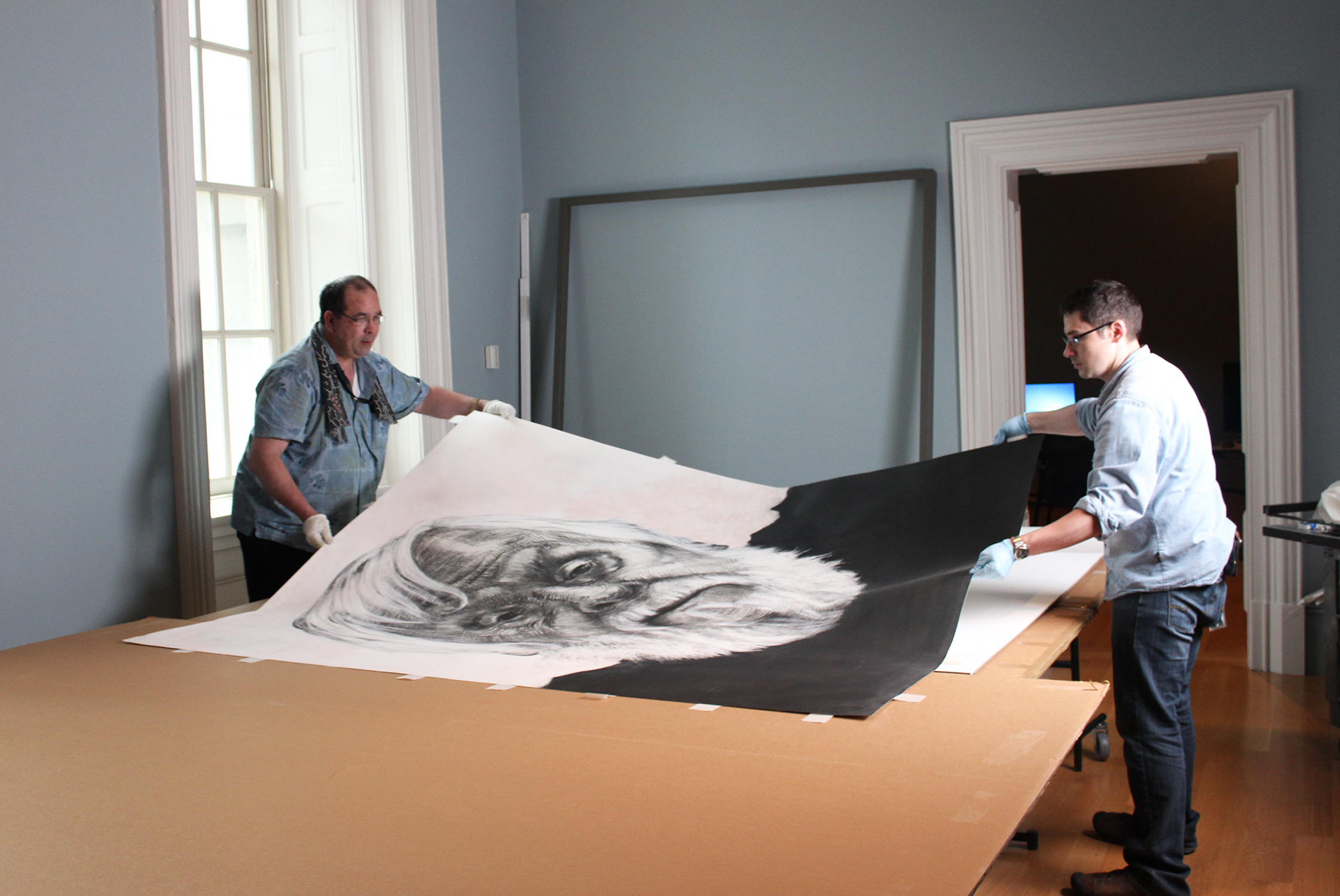 Museum workers working on installing large portrait