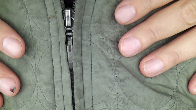 Close-up of hands on green jacket, one hand on each side of the zipper