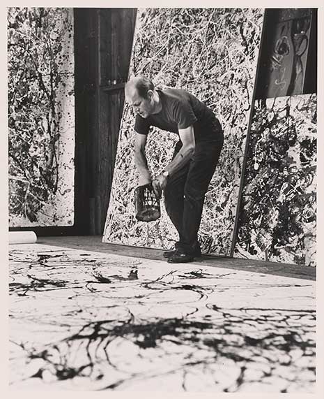 Jackson Pollock painting, with his canvas on the ground, and paint bucket in hand