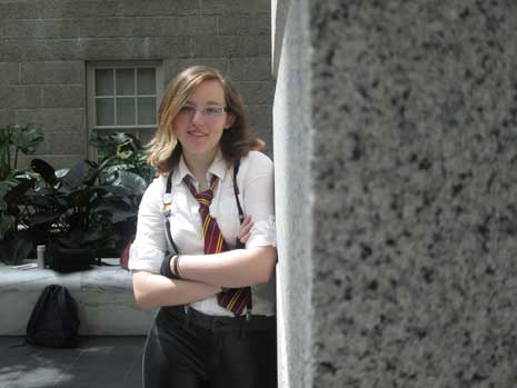 Kat McGrail in dress shirt, tie, and suspenders, with arms folded and looking at camera