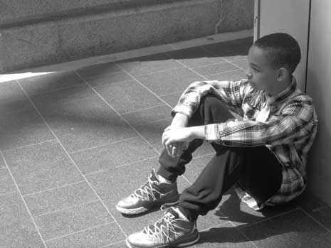 Black and white photo of Nekaijah Cordell in flannel shirt, sitting against wall