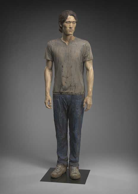 Full length wooden sculpture of Seqouyah Aono, wearing jeans, t-shirt, and tennis shoes
