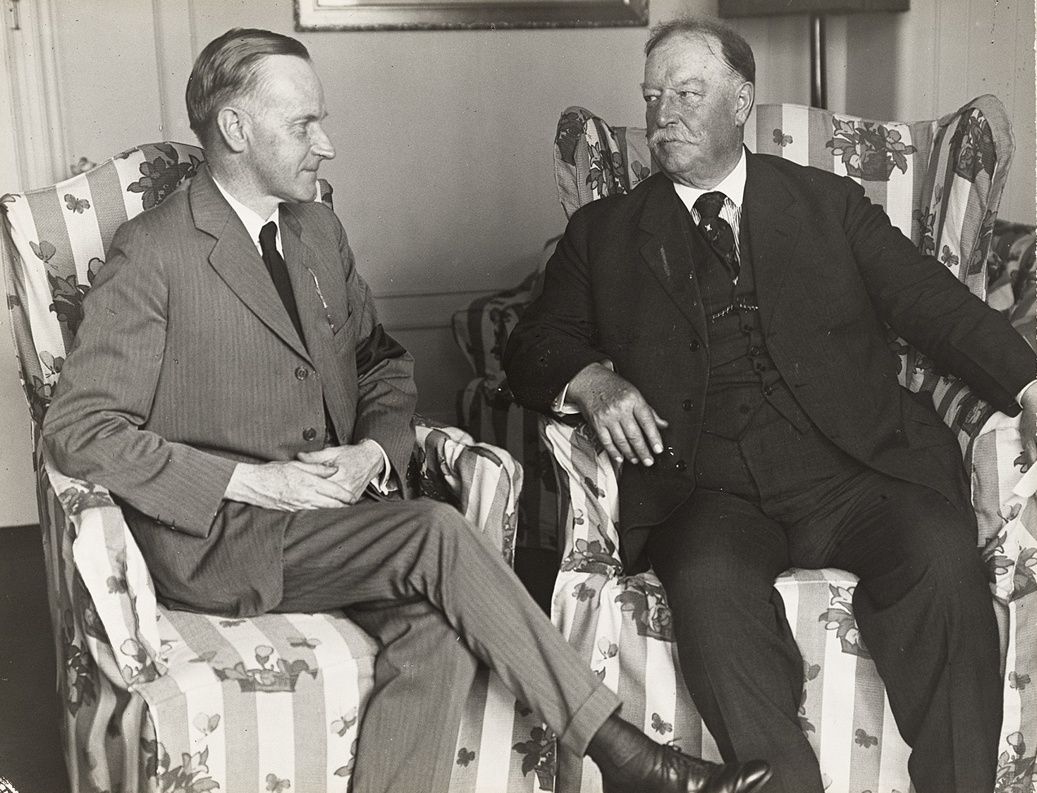 Two men sitting in flowered armchairs engaged in conversation