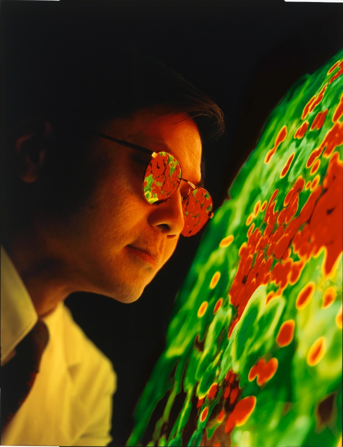 A man wearing light-protecting glasses looking at a projection of a large green and red mass