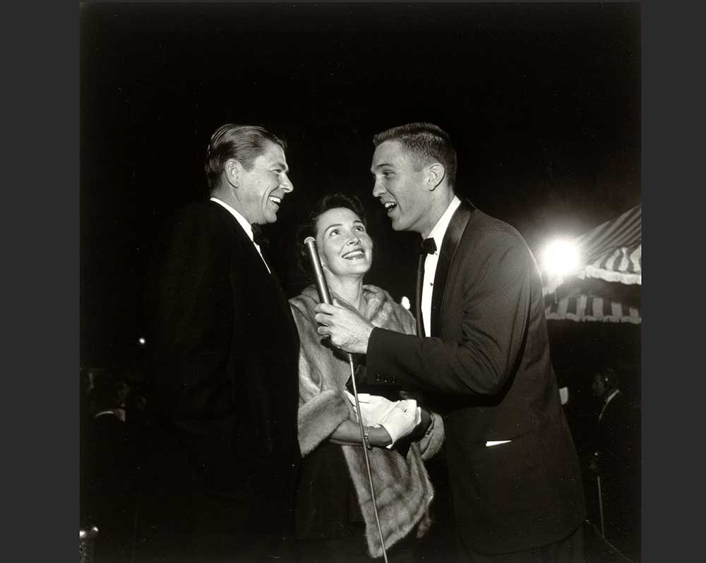 Two men in suits with a woman in a fur stole