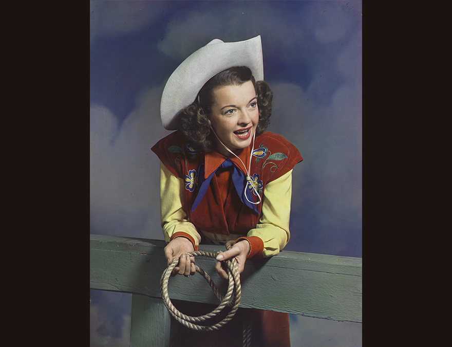 Woman in a cowgirl outfit leaning on a fence