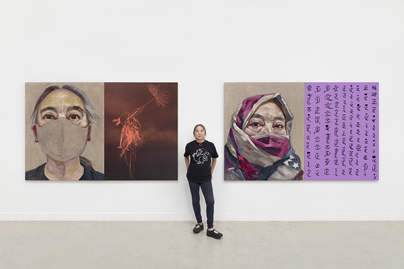 Artist in her studio between two large portraits