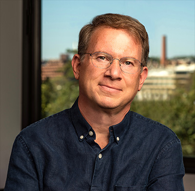 photo of a man in glasses in a blue shirt with the DC skyline in the background