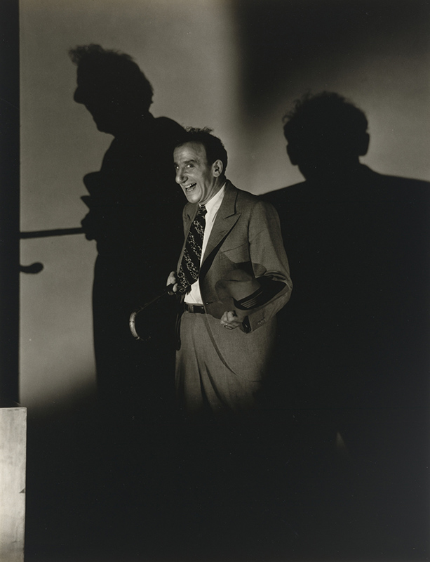 knee length photo of a laughing man with a cane and hat in deep shadow