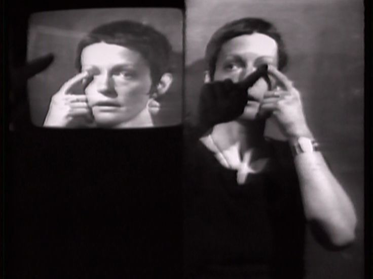 Black and white video of a woman with short hair pointing to her eyes