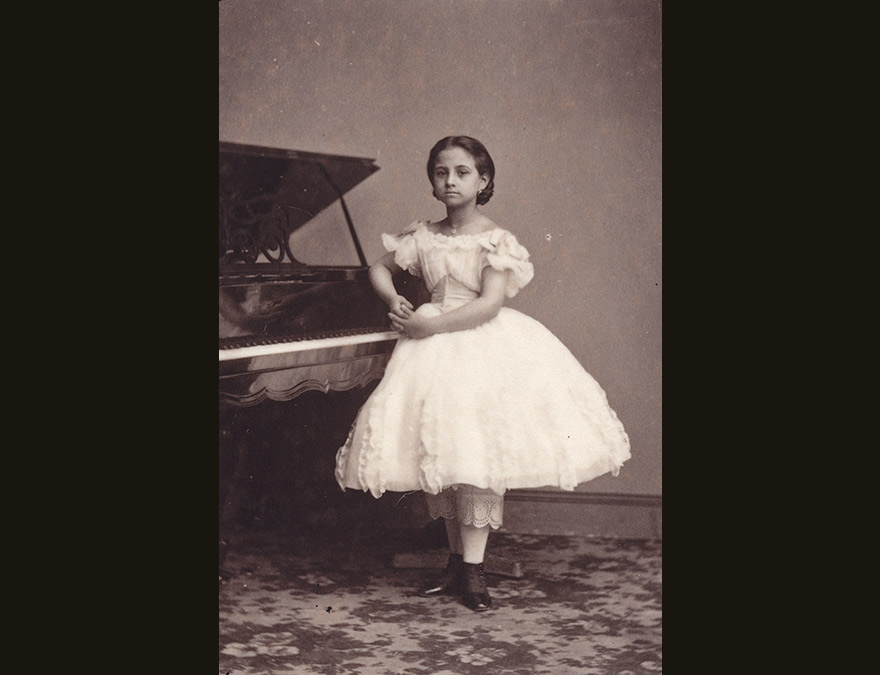 little girl in a white dress standing by a piano