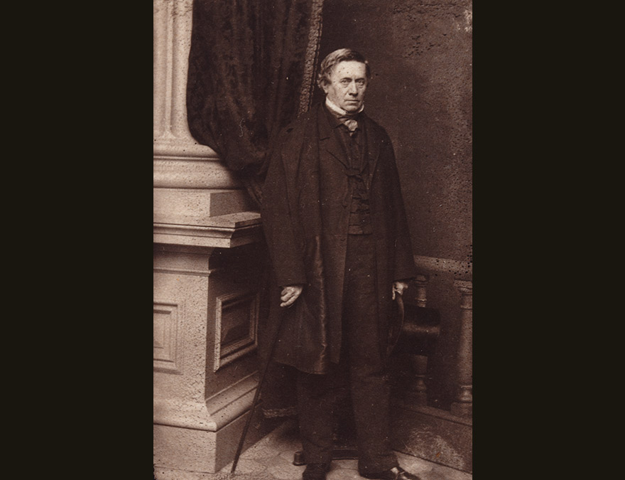 19th century man in a suit standing by a column