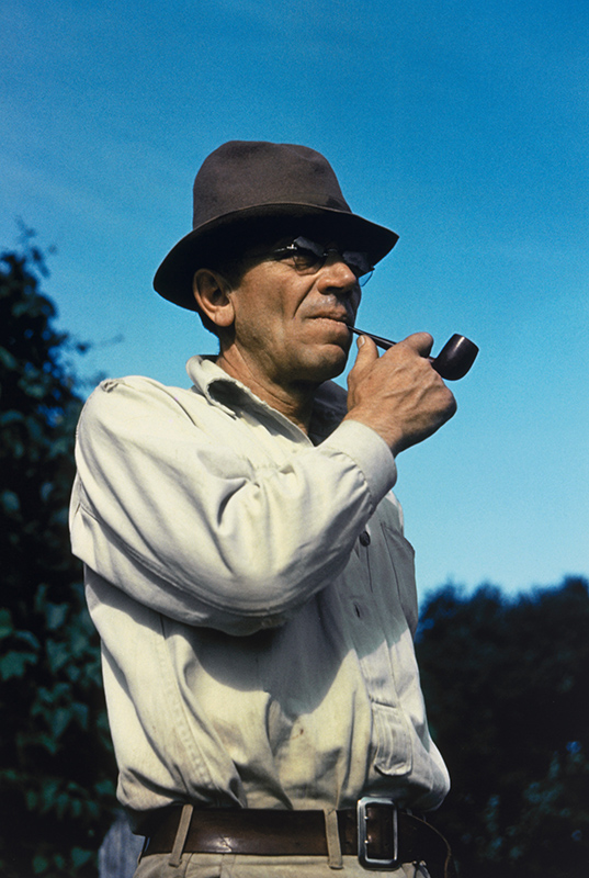 waist length photo of a man in a white shirt and a hat standing outdoors