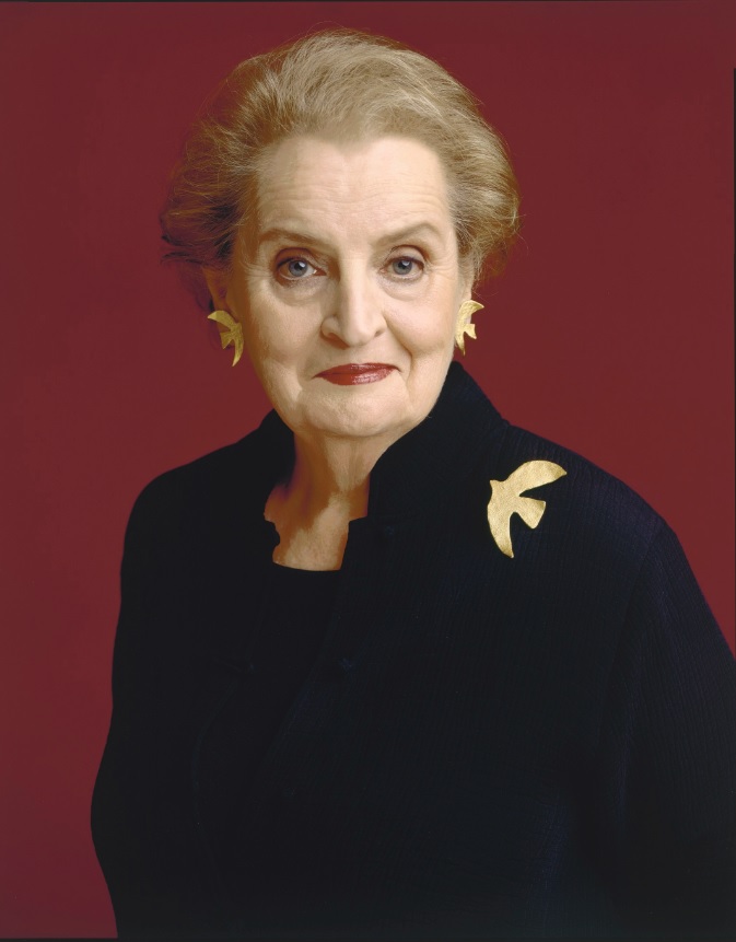 A photograph of a woman staring at the viewer wearing a black suit and a dove pin