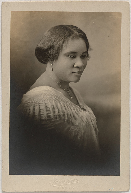 young Black woman facing right with her hair up-swept wearing a white dress