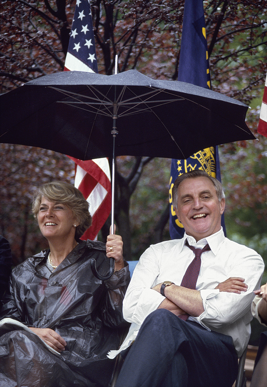 man and woman sitting in the rain, the woman holds an umbrella over the pair