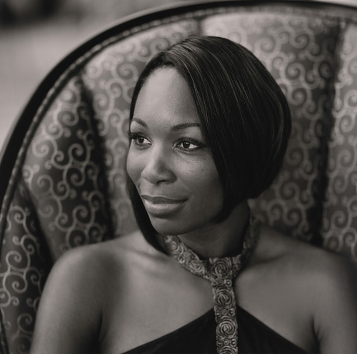 Venus Williams sits in a chair wearing a dress and smiling and looking to her right.
