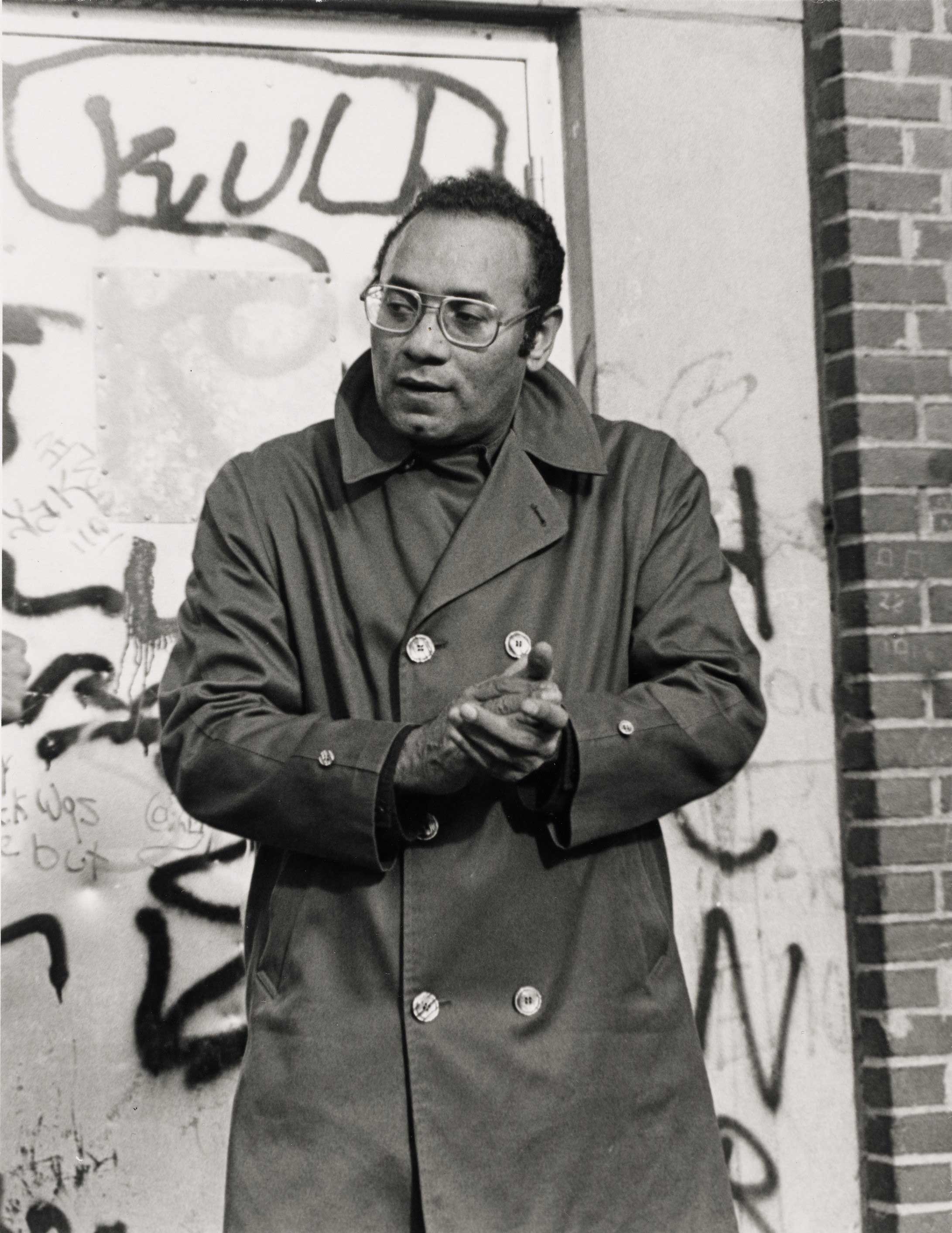 Black and white image of a man staring in the distance with his hands together