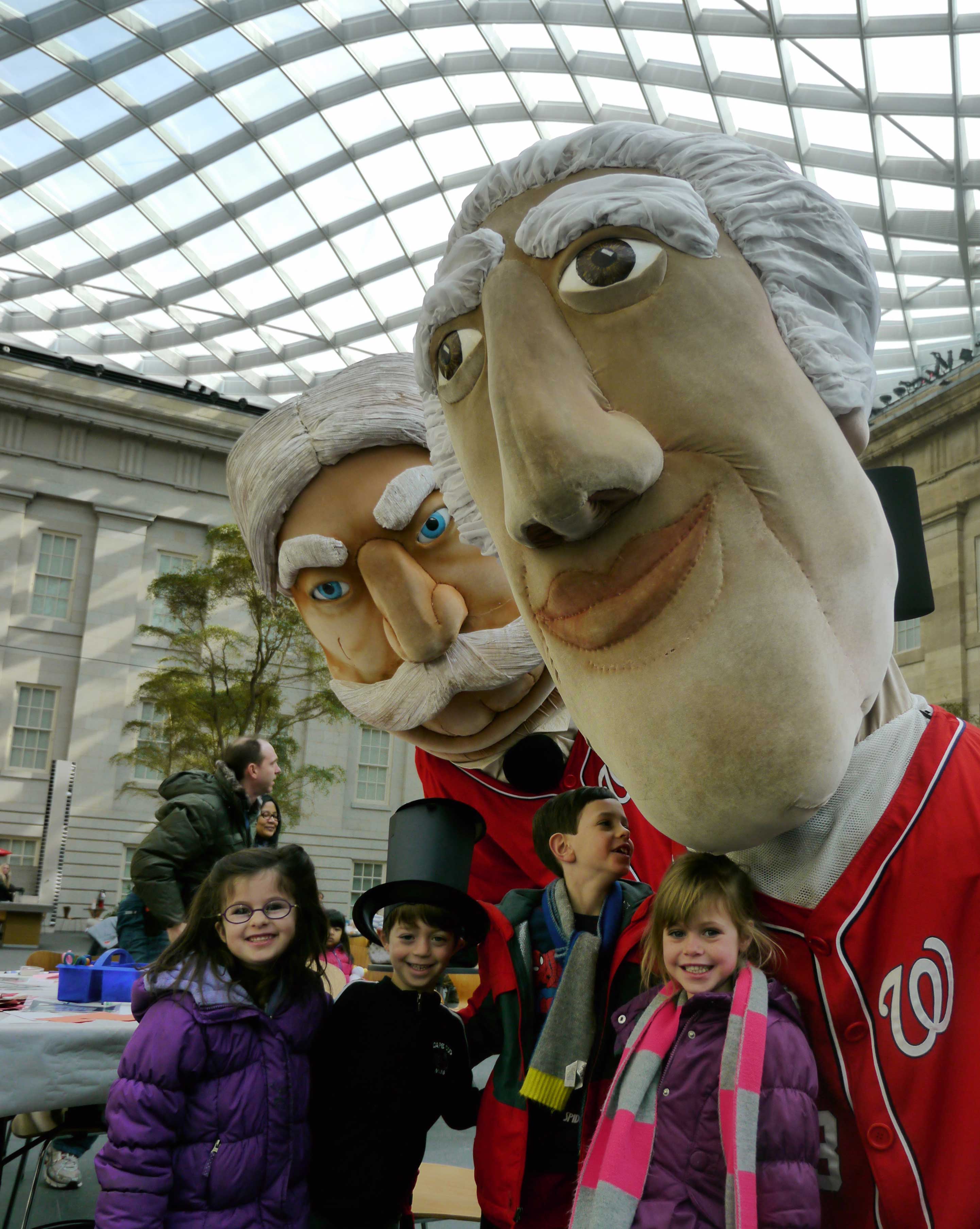 Children standing with large-headed president mascots wearing baseball jerseys