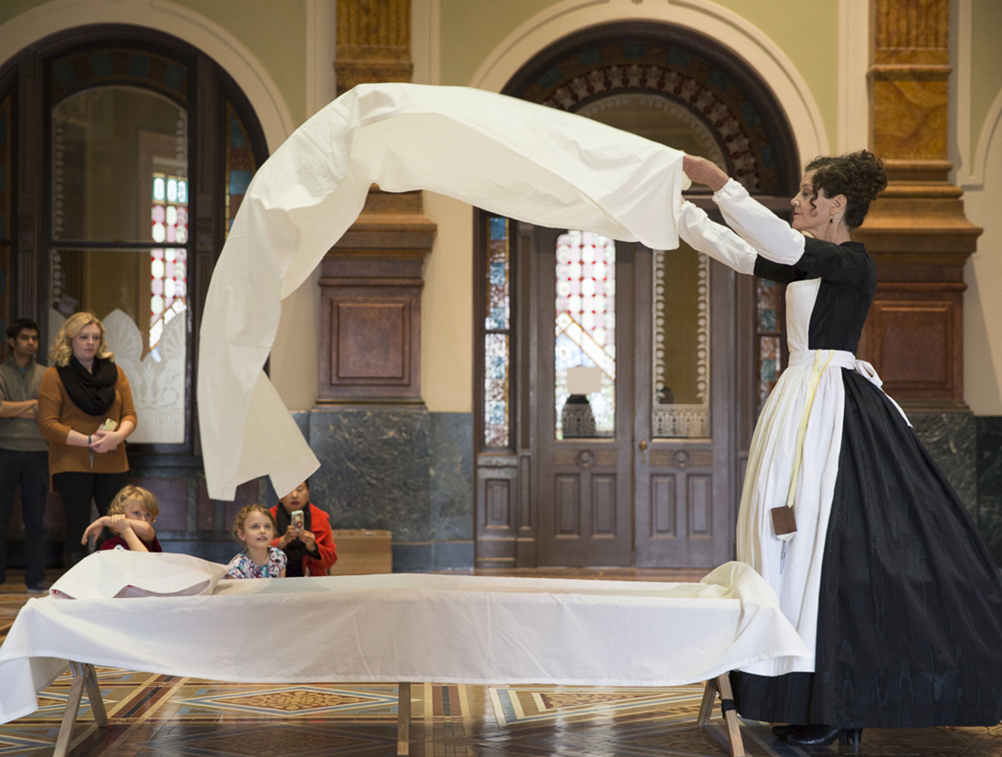 Woman throwing a sheet over a cot