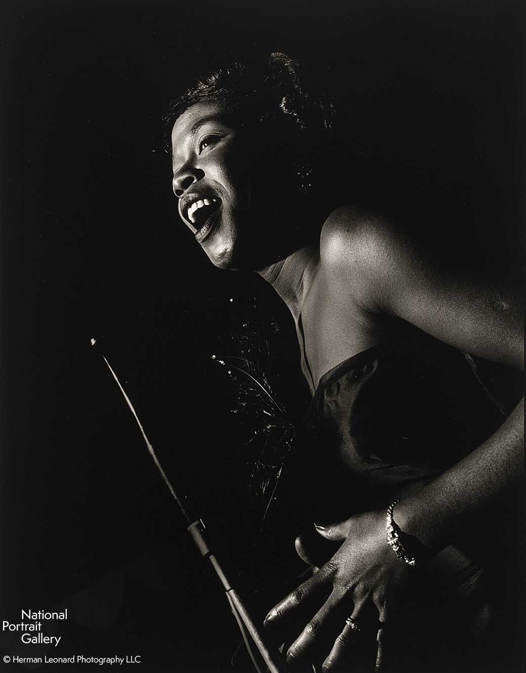 Black and white image of a woman standing in profile singing into a microphone