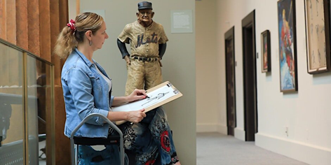 A woman looks at a framed piece of art with a clipboard and piece of charcoal in hand